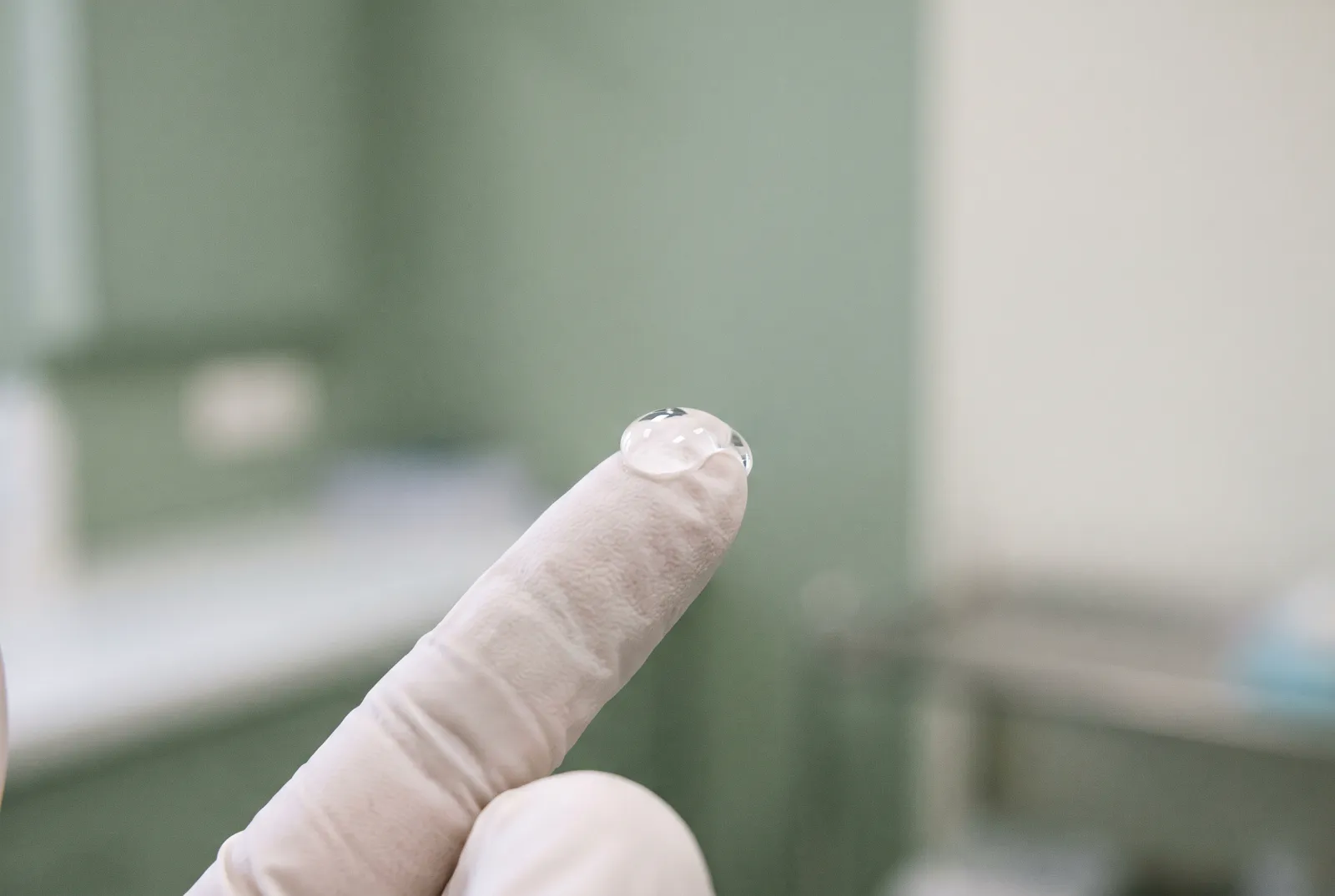 Gota de gel transparente sobre la yema de un dedo enguantado, vista muy de cerca sobre un fondo clínico claro