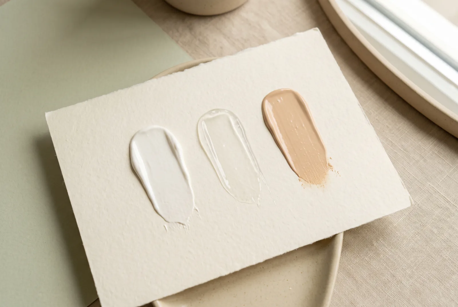 Tres muestras de protector solar en fila sobre papel: una blanca de filtro mineral, una transparente y una beige con color