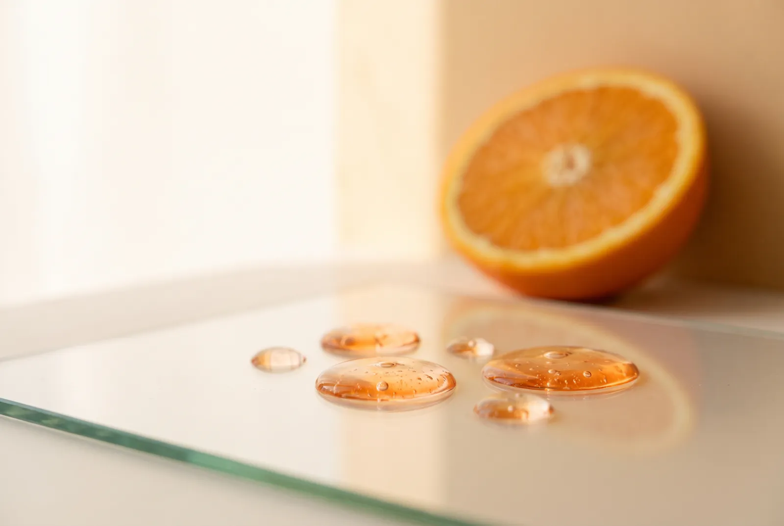 Gotas de sérum anaranjado sobre una lámina de vidrio, con media naranja desenfocada al fondo