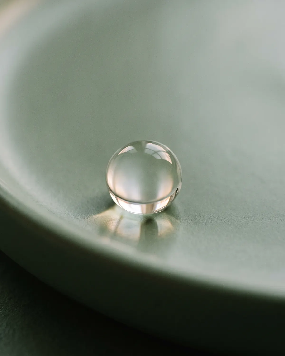 Una sola gota transparente sobre una superficie verde salvia.